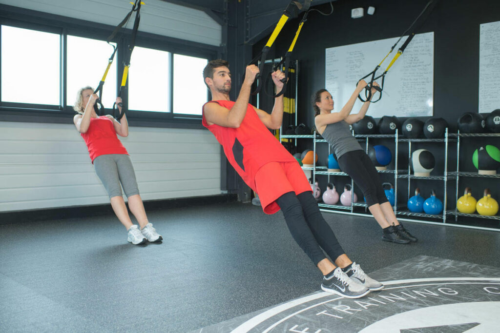 Three people training on suspension straps in a small group session